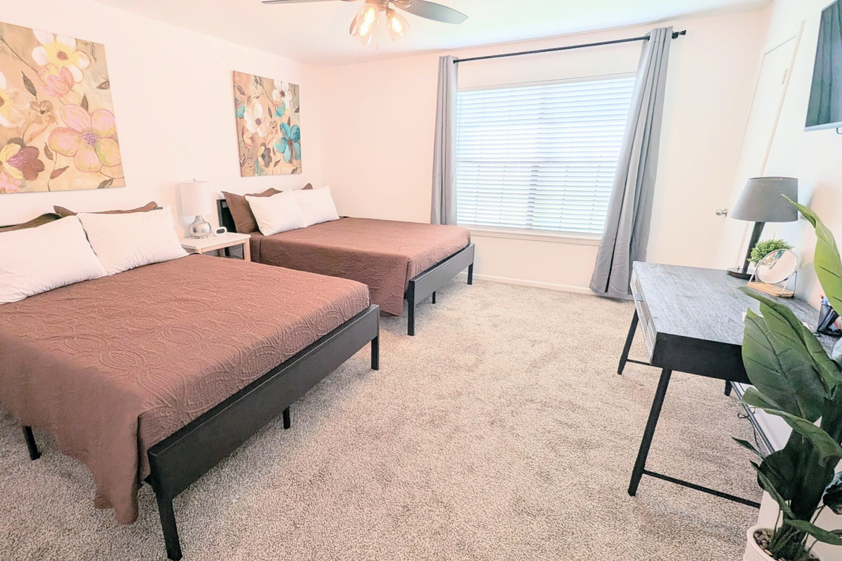 Queen bedroom features two queen beds, blackout curtains, a dedicated workspace, Roku TV, ceiling fan, and easy-access to charging stations. 