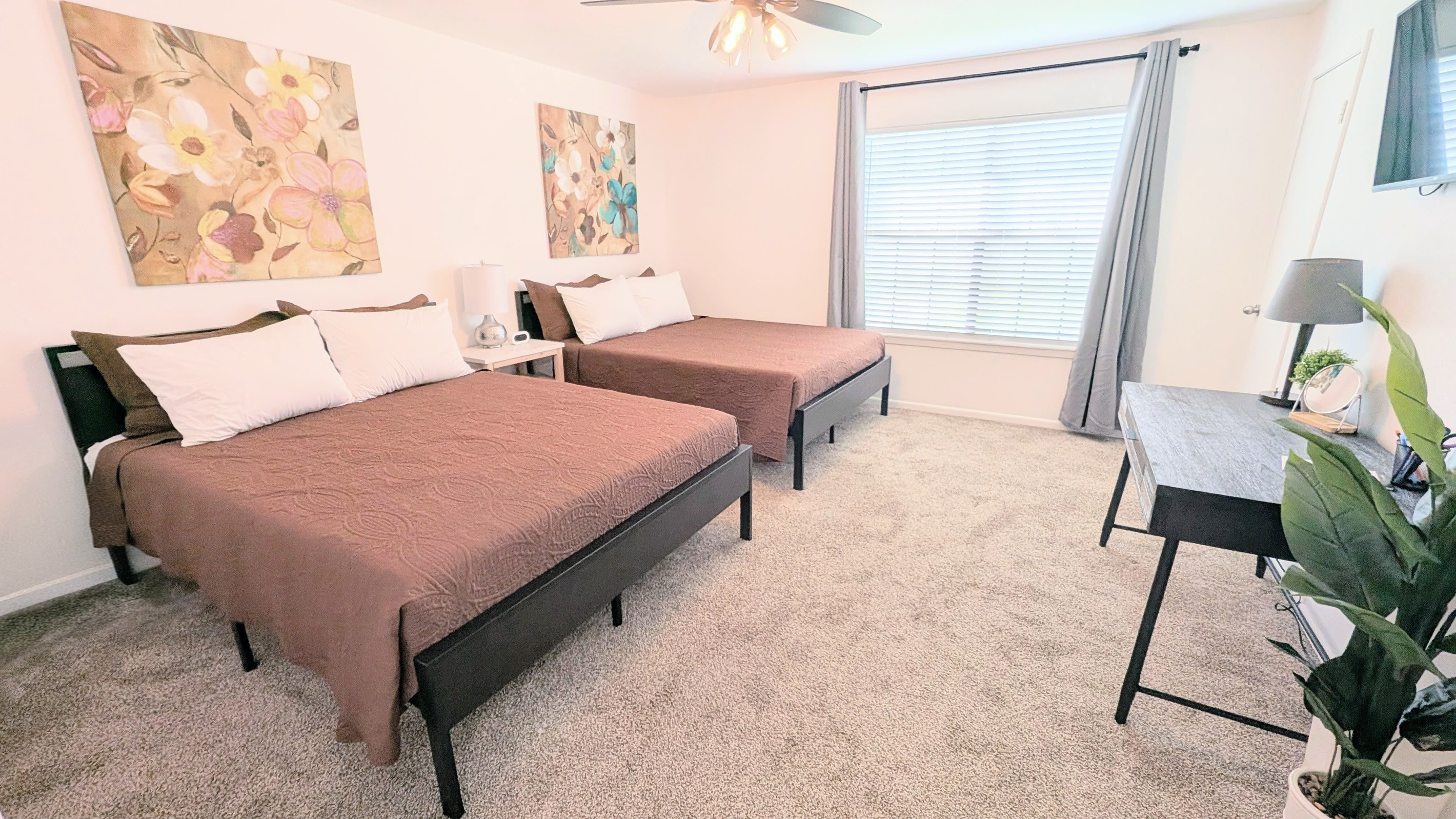 Queen bedroom features two queen beds, blackout curtains, a dedicated workspace, Roku TV, ceiling fan, and easy-access to charging stations. 