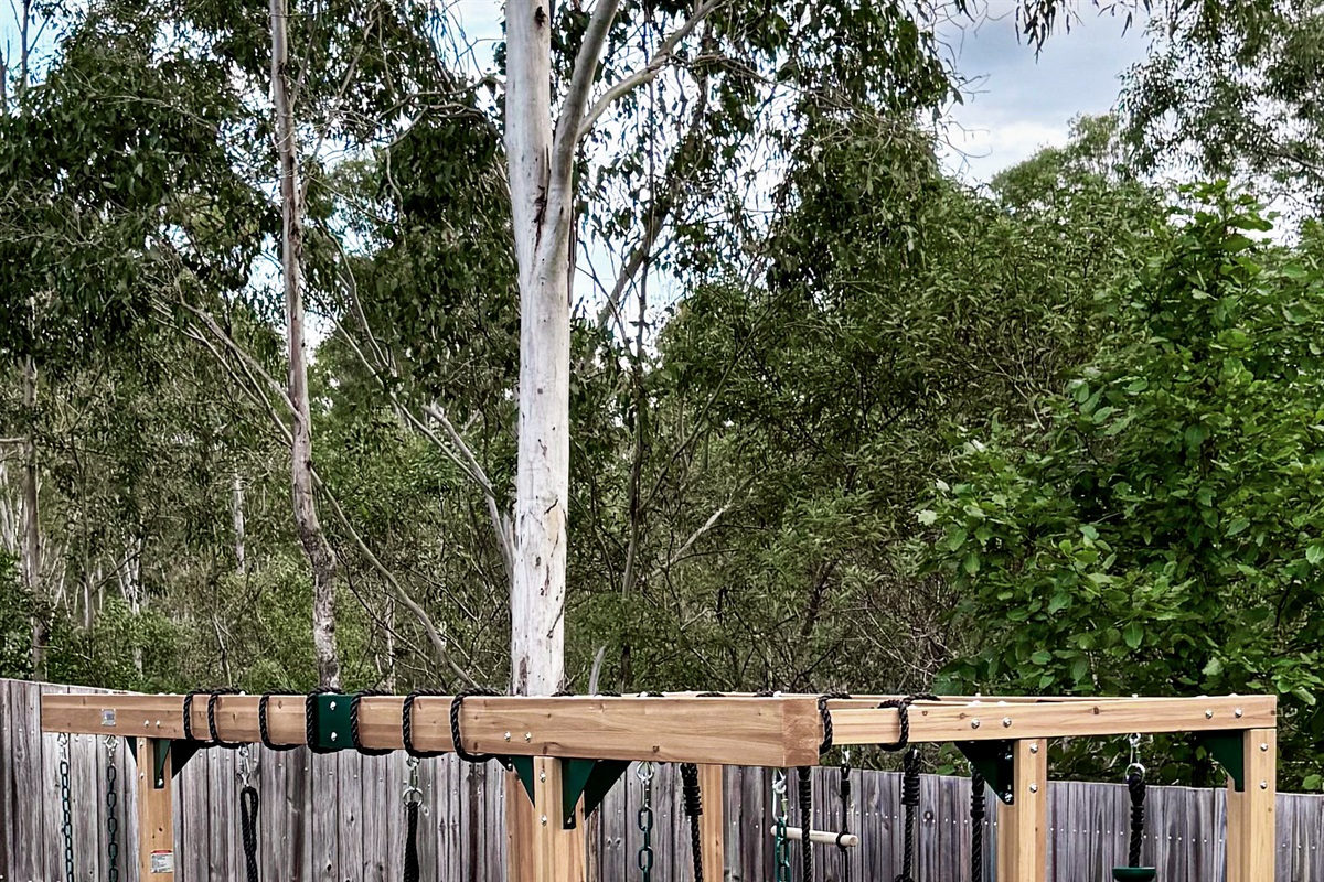 The jungle gym sits inside the fenced backyard, with swings, climbing sections and lawn space around the play structure.