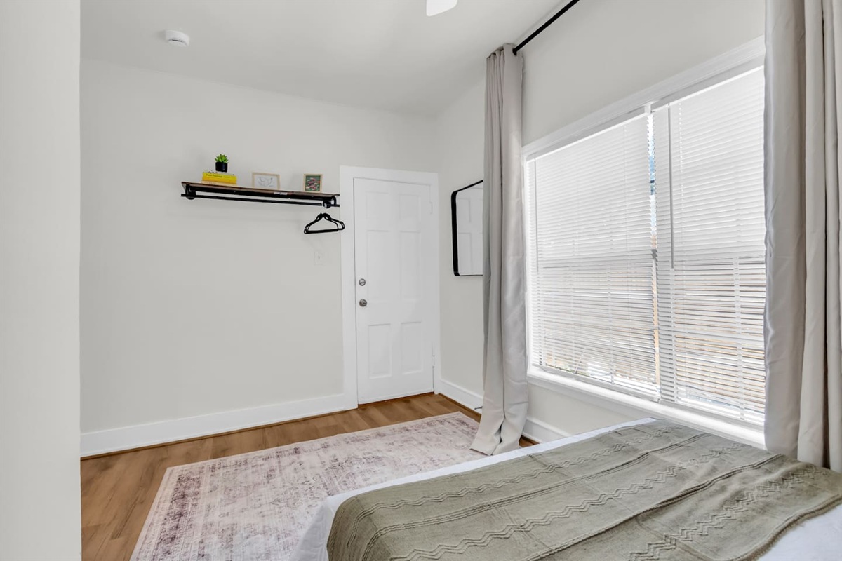 Queen bedroom with exposed closet with hangers, room darkening shades, and a large window.