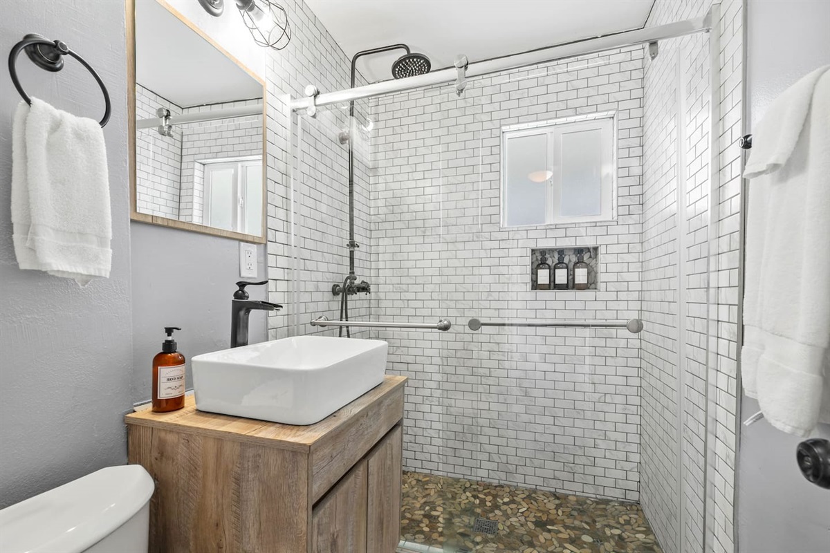 Sophisticated full bathroom featuring an elegant sink with a stylish faucet, a sleek mirror, and a glass door shower. Perfect lighting enhances the ambiance, creating a bright and relaxing space ideal for refreshing moments.