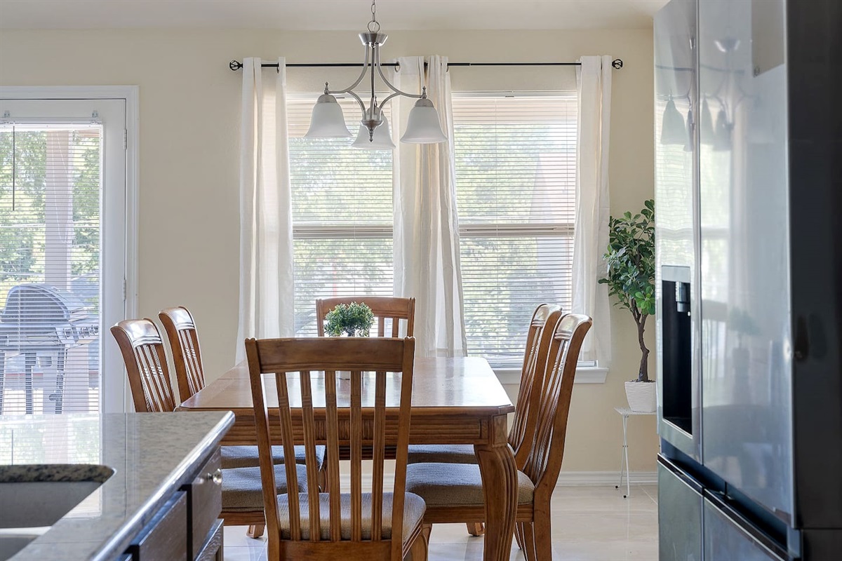 Step inside to see a light-filled, airy dining room featuring a traditional wooden table set, complemented by elegant lighting and wall art.