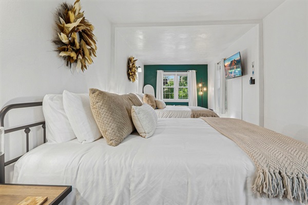Feather wreaths crown each queen bed, adding soft style. Cozy blankets, plush pillows, and bedside touches create a warm South Bend guest retreat near Notre Dame—perfect for restful nights.
