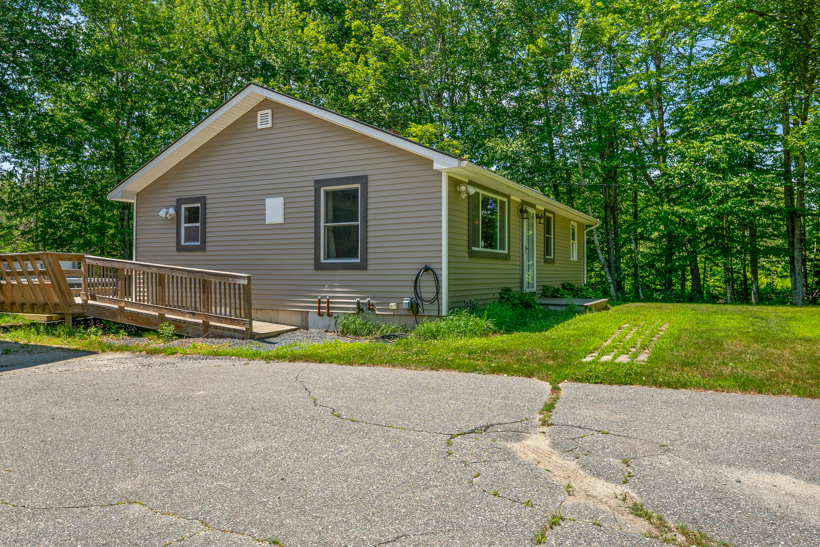 Charge overnight with the Level 2 EV charging station located right next to the driveway. View highlights the wooden entry ramp providing accessible entry up to the outdoor deck and the main side entry door of this ranch-style home.