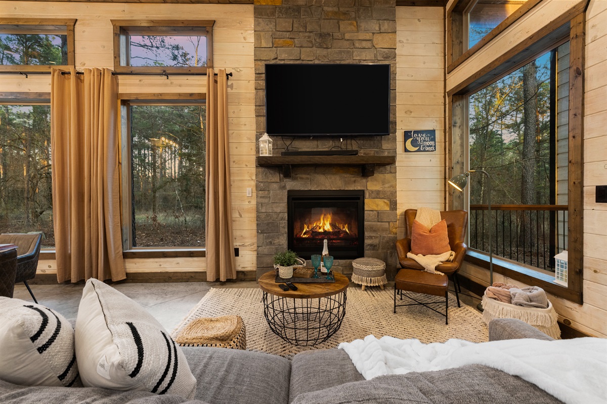 Settle into plush seating as twilight settles over the forest in the living room. The fireplace glows, the TV is ready for the game, and the whole space feels made for cozy nights in.