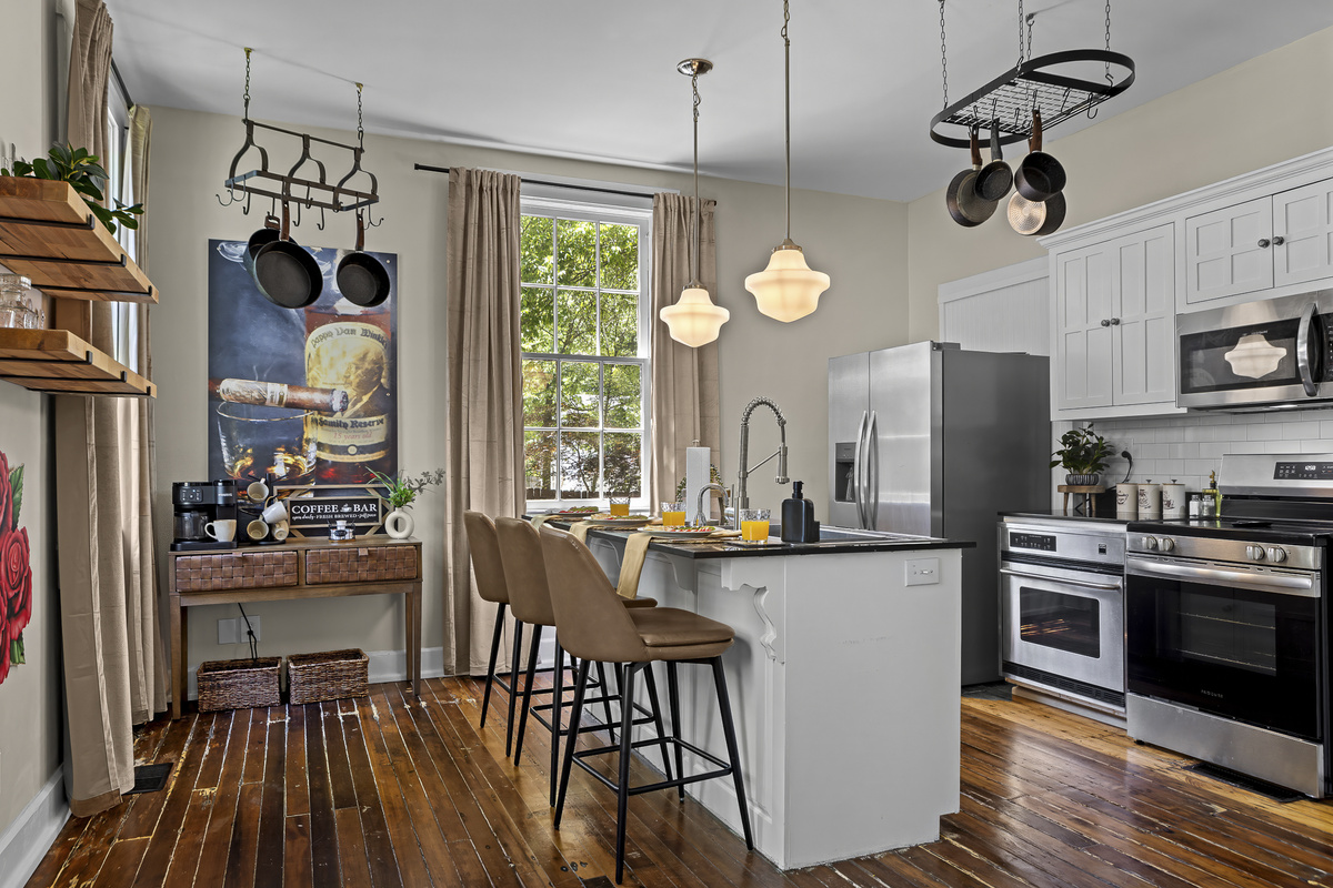 A fully stocked kitchen with island bar seating, a hanging pot rack, stainless appliances, and a dedicated coffee station.
