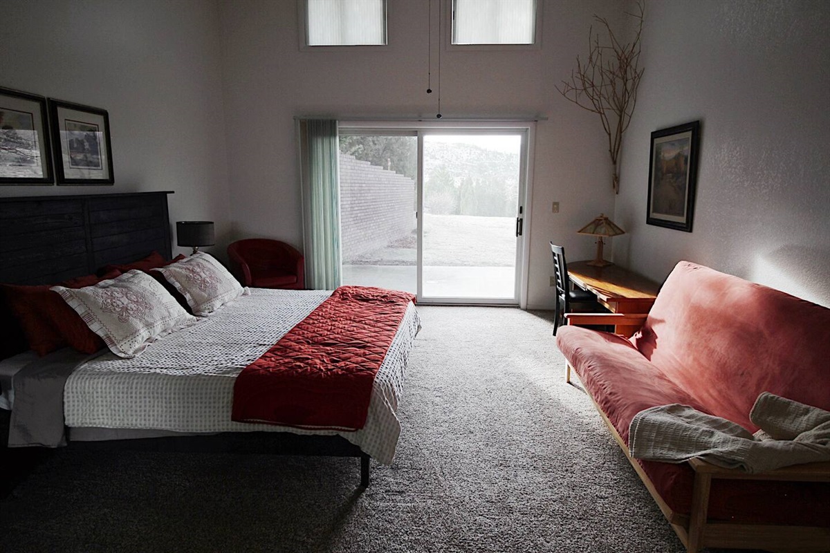 As you embrace the serenity of this thoughtfully designed space, the bed, colors, glass door, couch, and red chair create an oasis of relaxation and beauty.