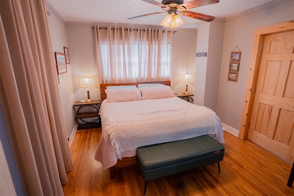 King bedroom featuring a wall-mounted smart TV, modern lighted vanity, and cozy bedding. Bright, functional setup for relaxing or getting ready.