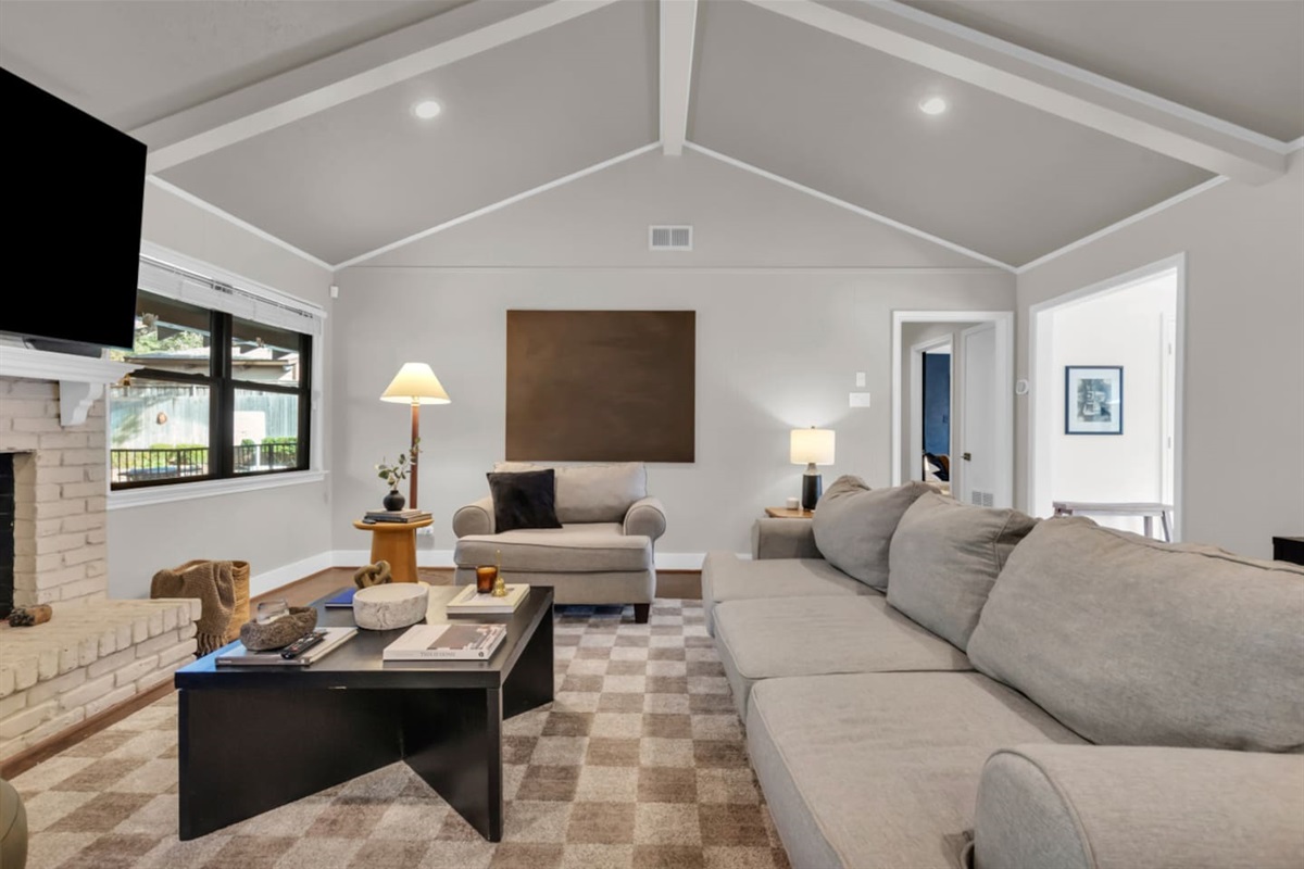 Luxe living room with a 70” Smart TV, cozy fireplace, ample seating, and an open-concept layout flowing into the fully equipped kitchen and coffee bar.