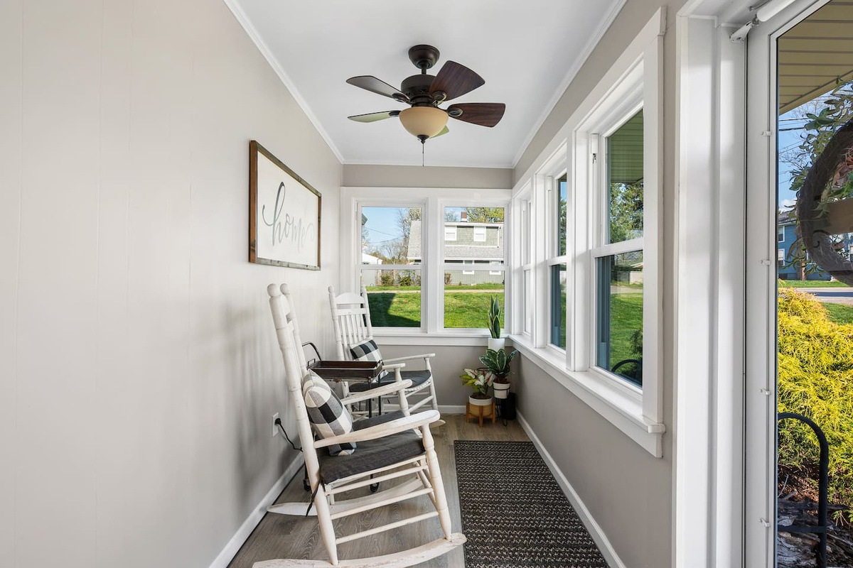 Bright sunroom with windows on two sides, comfortable seating, and a classic rocking chair.