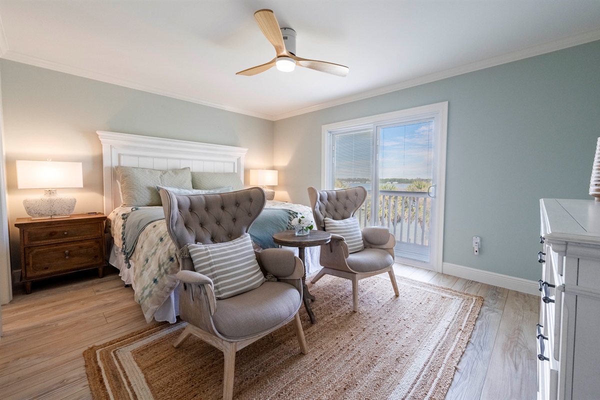 Elegant bedroom with a king-sized bed, warm natural light, cozy seating, and a balcony ideal for peaceful starts and sunset unwinding.