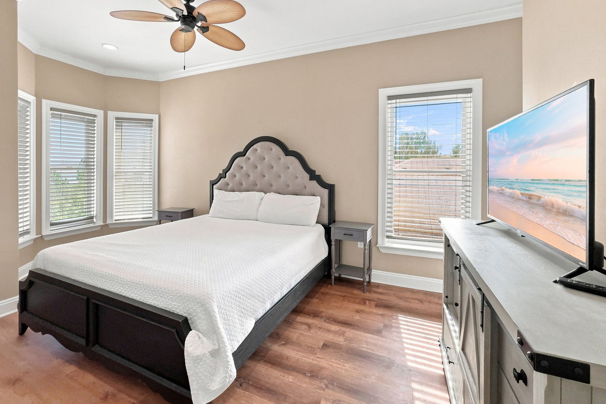 Bedroom with an upholstered headboard, smart TV, and corner windows