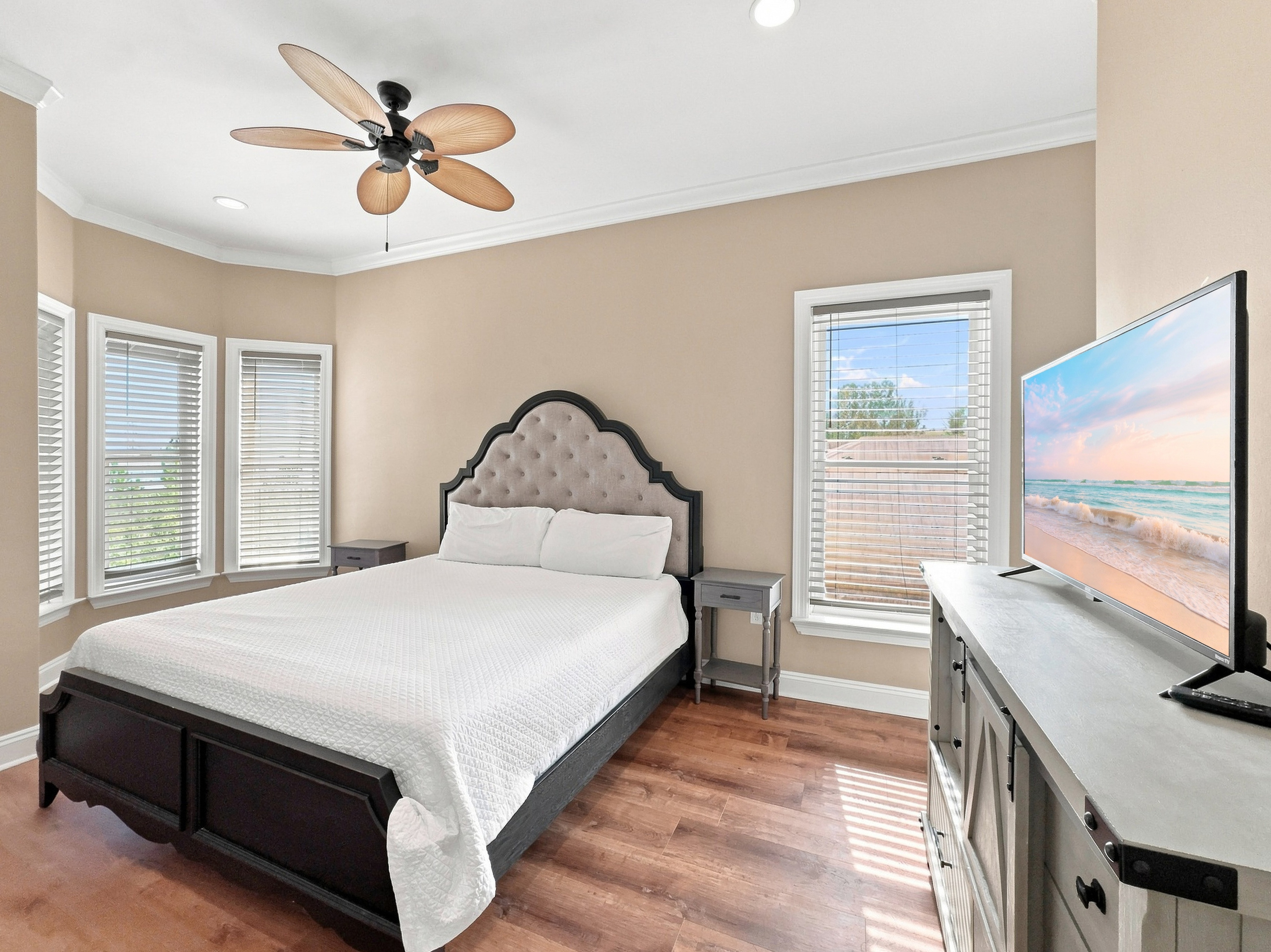 Bedroom with an upholstered headboard, smart TV, and corner windows