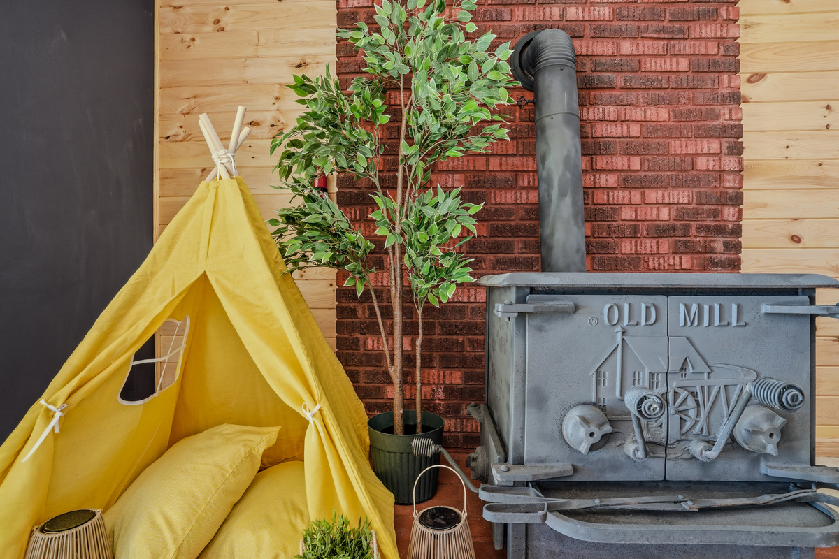 Lower-level den with yellow teepee accent, potted tree, and vintage Old Mill wood stove (decorative purposes only)