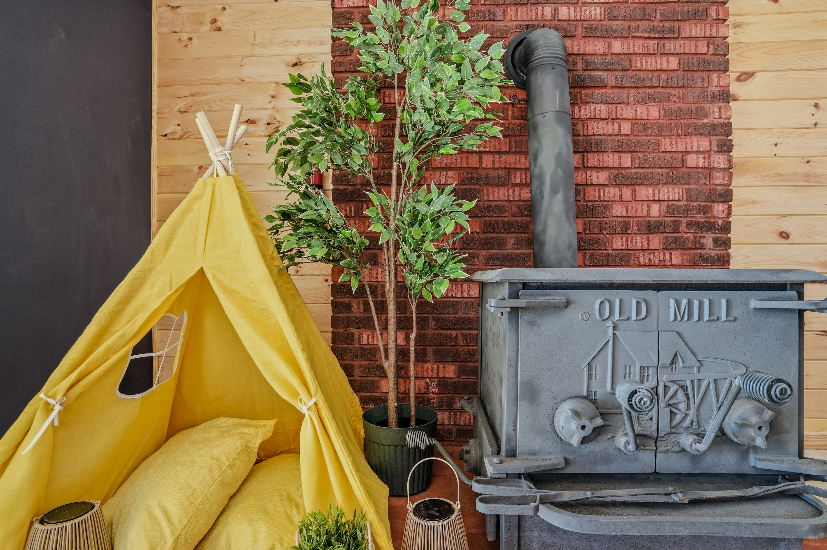 Lower-level den with yellow teepee accent, potted tree, and vintage Old Mill wood stove (decorative purposes only)