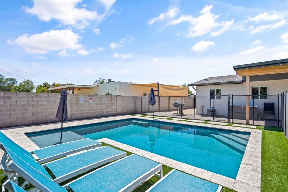 Private backyard pool with safety fence, lounge chairs, umbrella shade, fire pit seating, and a bright outdoor space 