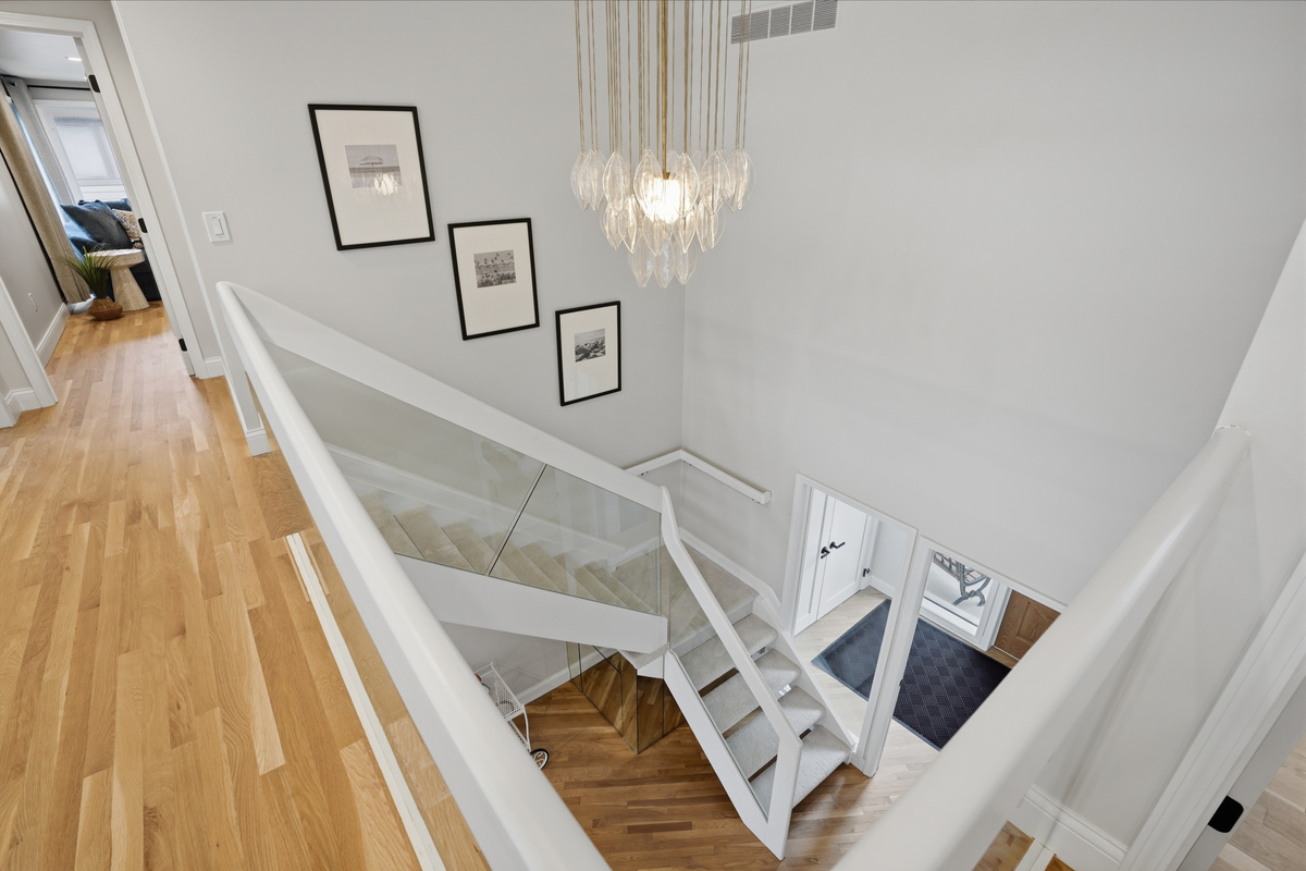 Bright, modern staircase with open railing, hardwood floors, and elegant chandelier lighting. Clean, airy design that enhances the home’s open and upscale feel.