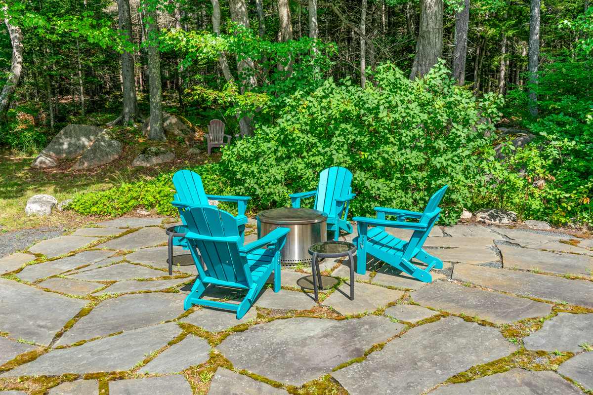 Your evening retreat. "The Crag's" wide stone patio features a smokeless fire pit, drink caddies, and vibrant seating—with additional woodland seats tucked directly into the trees of Acadia for quiet moments under the stars.
