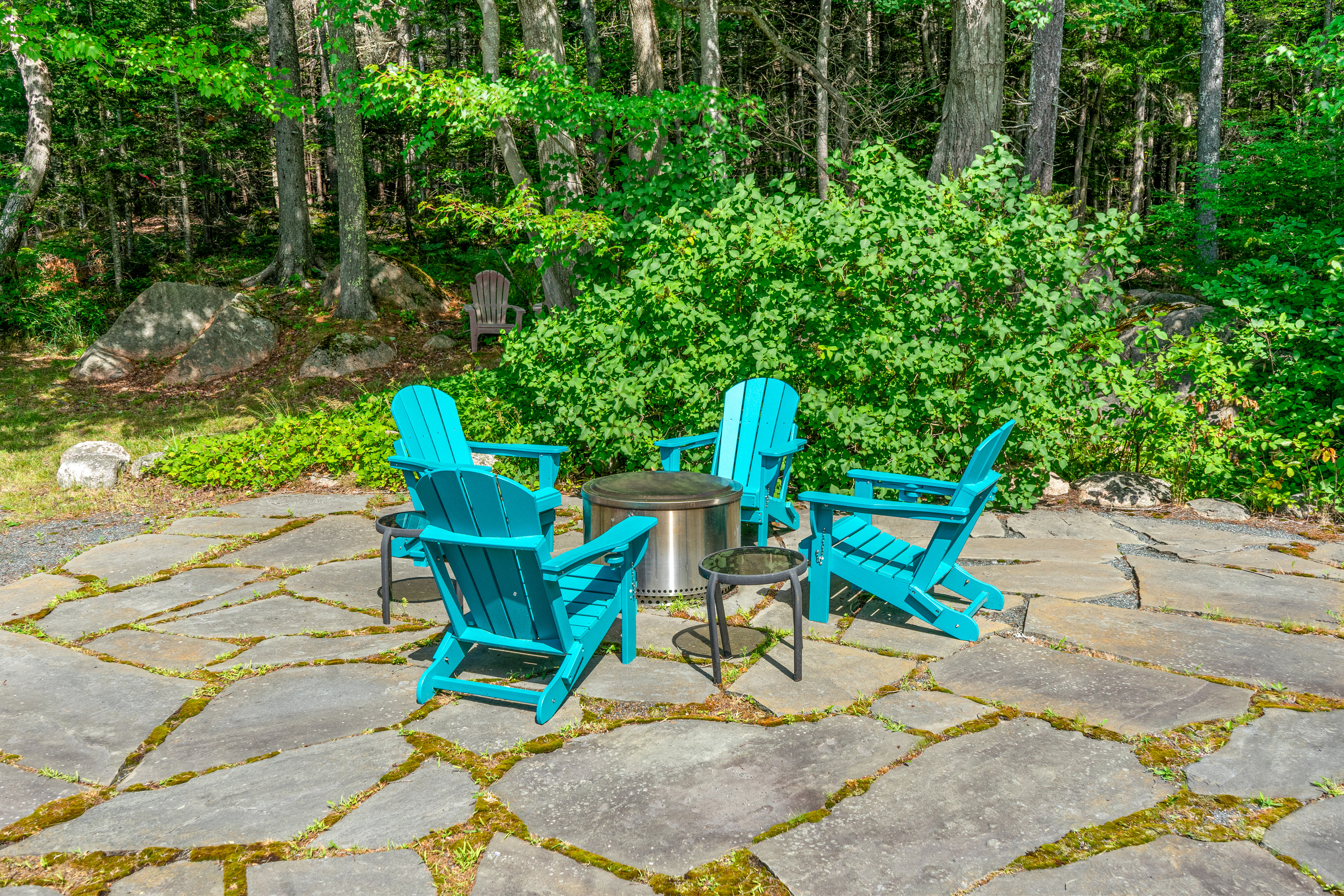 Your evening retreat. "The Crag's" wide stone patio features a smokeless fire pit, drink caddies, and vibrant seating—with additional woodland seats tucked directly into the trees of Acadia for quiet moments under the stars.