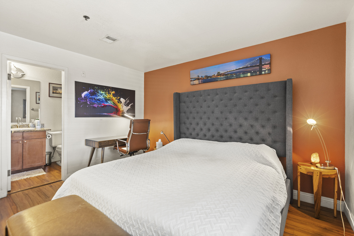 Bedroom 1 with king bed, full bathroom access, desk workspace, and warm accent wall.
