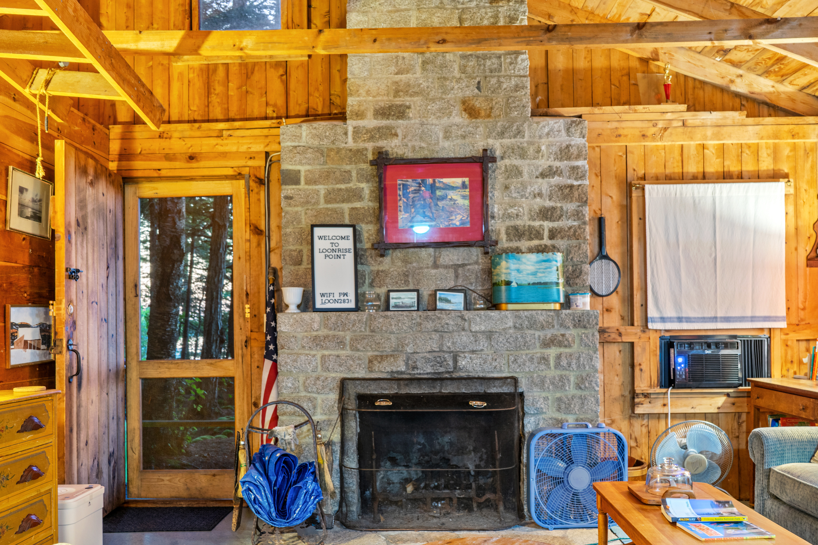 Stone masonry focal point at Loonrise Point! Features welcome sign with Wi-Fi details, window AC unit, and screened porch door. Please note: Fireplace is decorative only and off-limits for guest use. Rustic interior charm on Beech Hill Pond, ME!