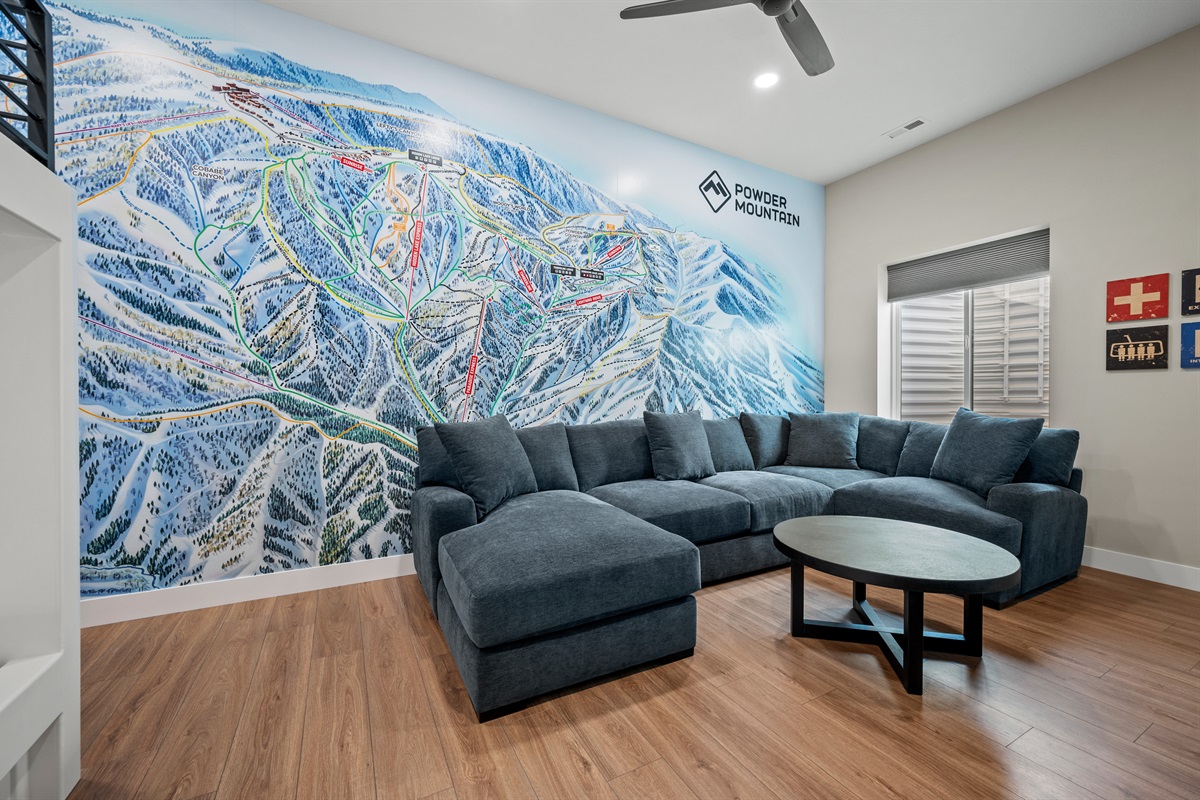A detailed Powder Mountain trail map adorns the wall behind the sectional, adding a touch of local adventure to the bunkroom lounge.