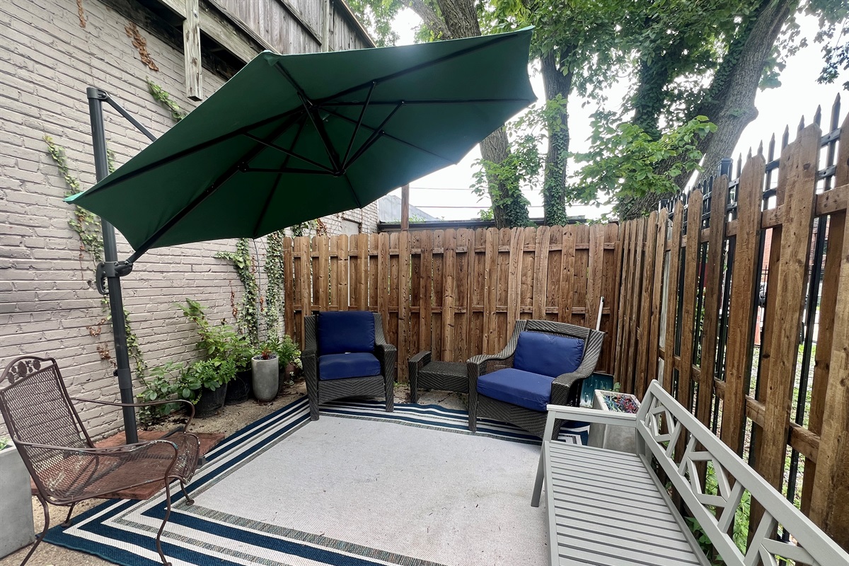 Inviting outdoor patio with shaded umbrella, comfy seating, and a private fenced backdrop