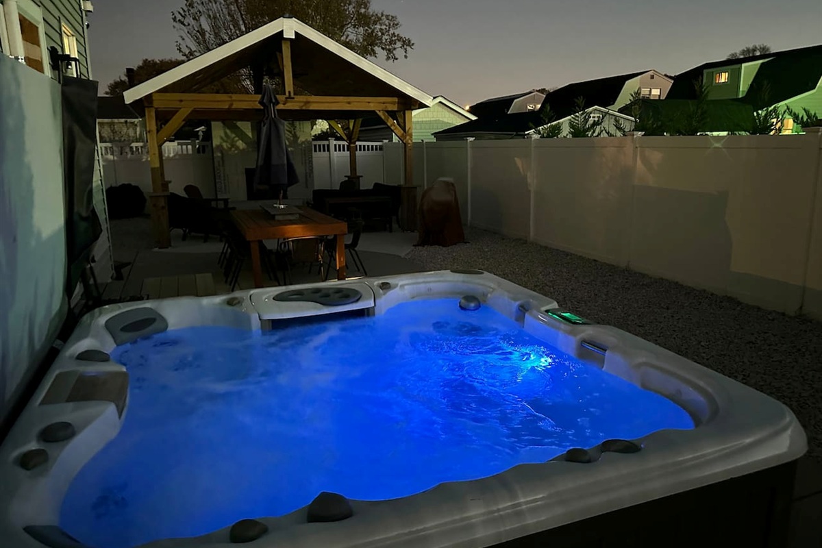 Indulge in ultimate relaxation under the stars in our glowing blue hot tub. This private backyard oasis features a spacious patio with a dining table and a covered lounge, perfect for soothing escapes during your vacation.