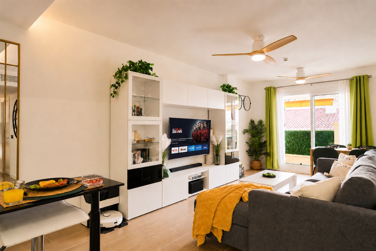 Stylish open-plan living room with a modern kitchen, smart TV, and natural light throughout — ideal for relaxing or sharing a glass of wine after a day by the beach.