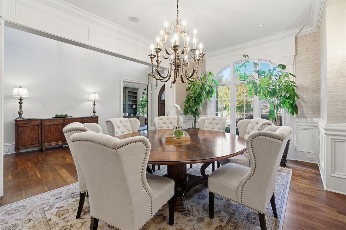 Spacious main dining room to the left of the foyer, featuring a chandelier, seating for seven, and lush green plants. A bright, welcoming space perfect for shared meals or special gatherings.