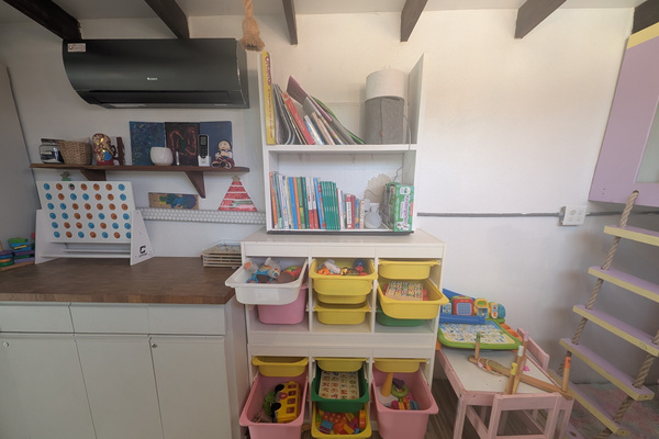 Indoor kids toy and craft station at Villa Coral featuring organized bins with toddler learning toys, books, a large wooden Connect Four game, and a small pink activities table in Dorado, Puerto Rico.