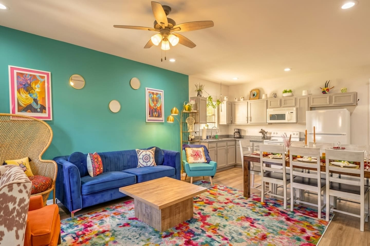 Bright, colorful downstairs living area with cozy seating, vibrant decor, dining table for 12, & a fully equipped kitchen with a 2nd coffee maker, microwave, hot plate, fridge, freezer, and sink.  No oven or range, which are available upstairs.
