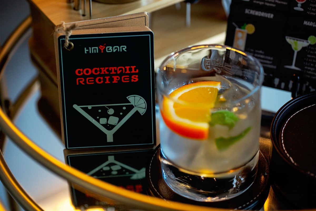 A close-up of a stylish bar cart, showcasing a custom-made cocktail recipe book and a refreshing drink with an orange slice and mint garnish. The setup is perfect for entertaining guests and creating custom drinks.