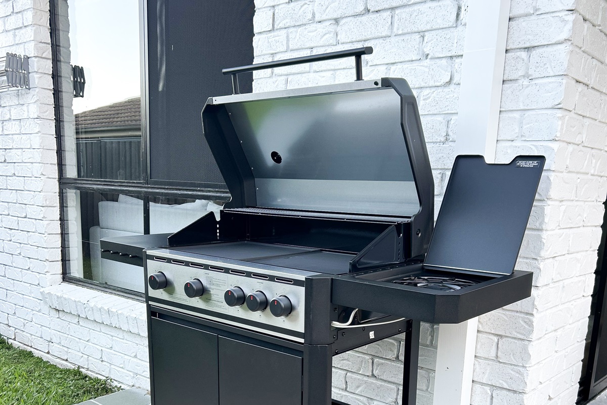 Summers Green View Retreat in Logan Reserve includes a 4-burner gas BBQ set beside the patio and backyard greenery.