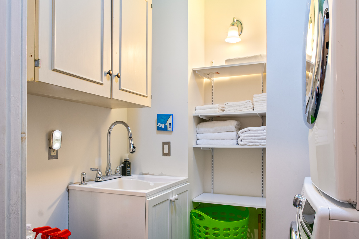 Convenient amenities at "The Crag." The dedicated laundry room features stacked washer and dryer units, a utility sink with a high-arc faucet, overhead storage, and fully stocked towel shelving for easy cleanup after Acadia hikes.