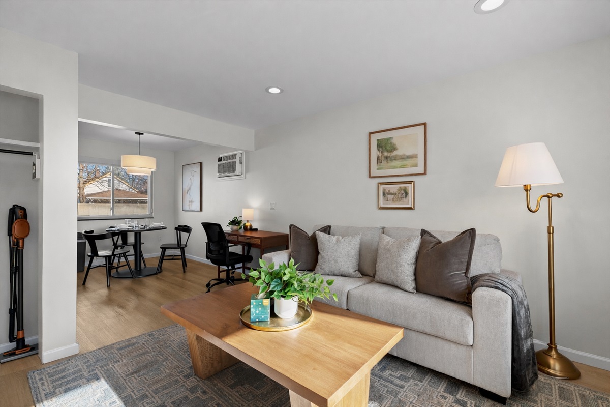 Comfortable, sunlit living space with plush seating, warm wood accents, and an open layout that flows seamlessly into dining and work areas.