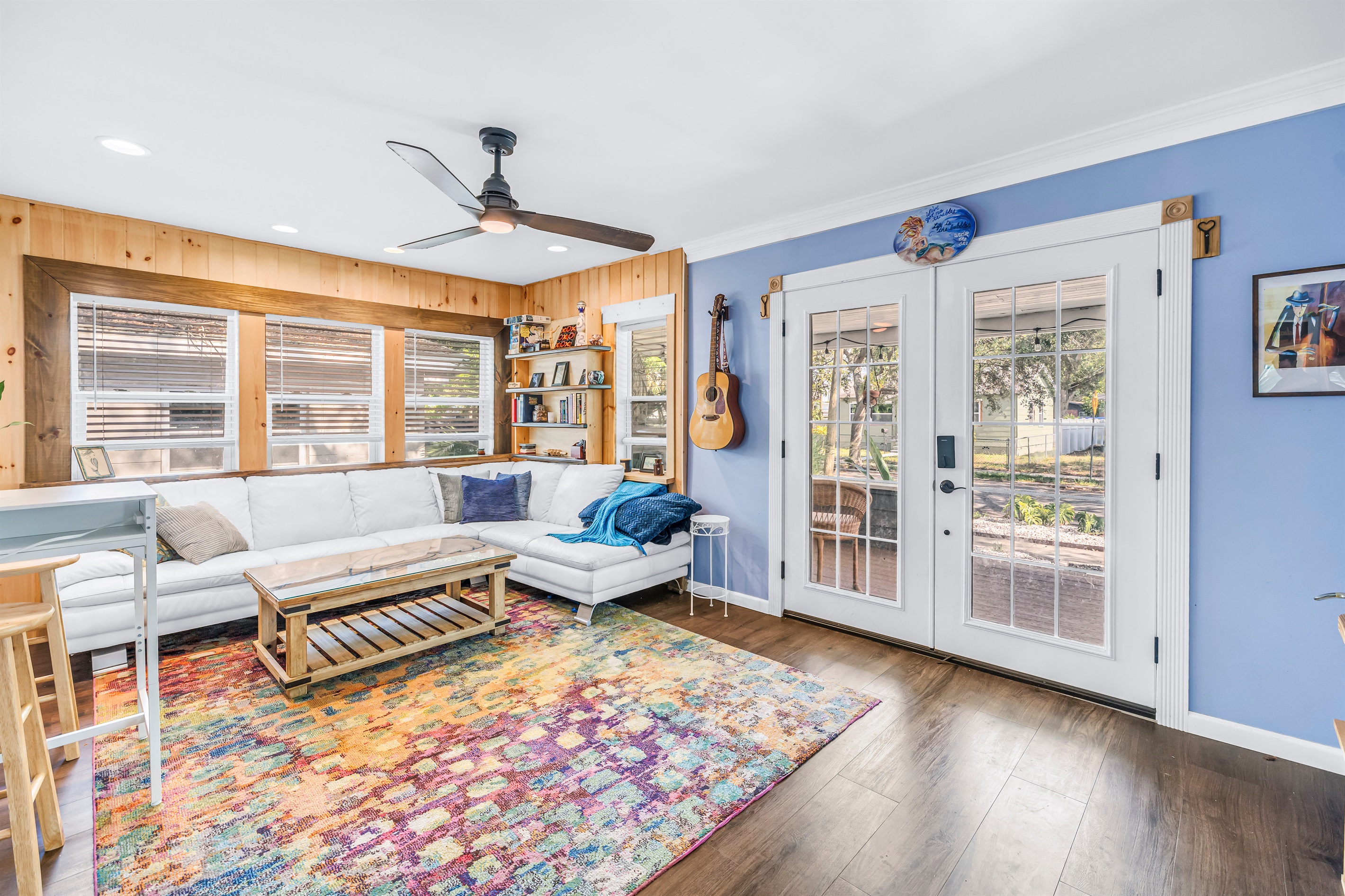 Bright and inviting living room with cozy seating, colorful area rug, ceiling fan, and French doors overlooking the outdoor space.