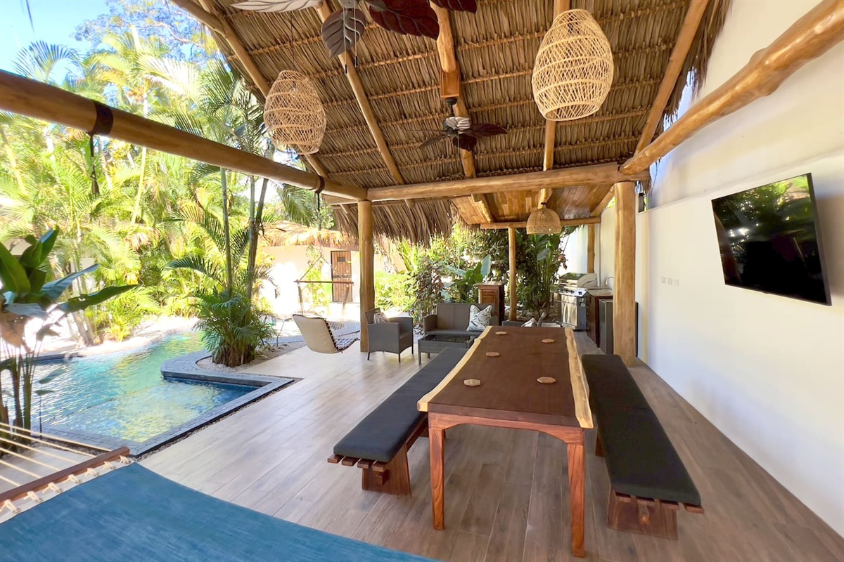 The Grand Cabana has a large dining table, two person hammock, sitting area, two swing chairs, gas grill, sink and 55 inch smart TV.