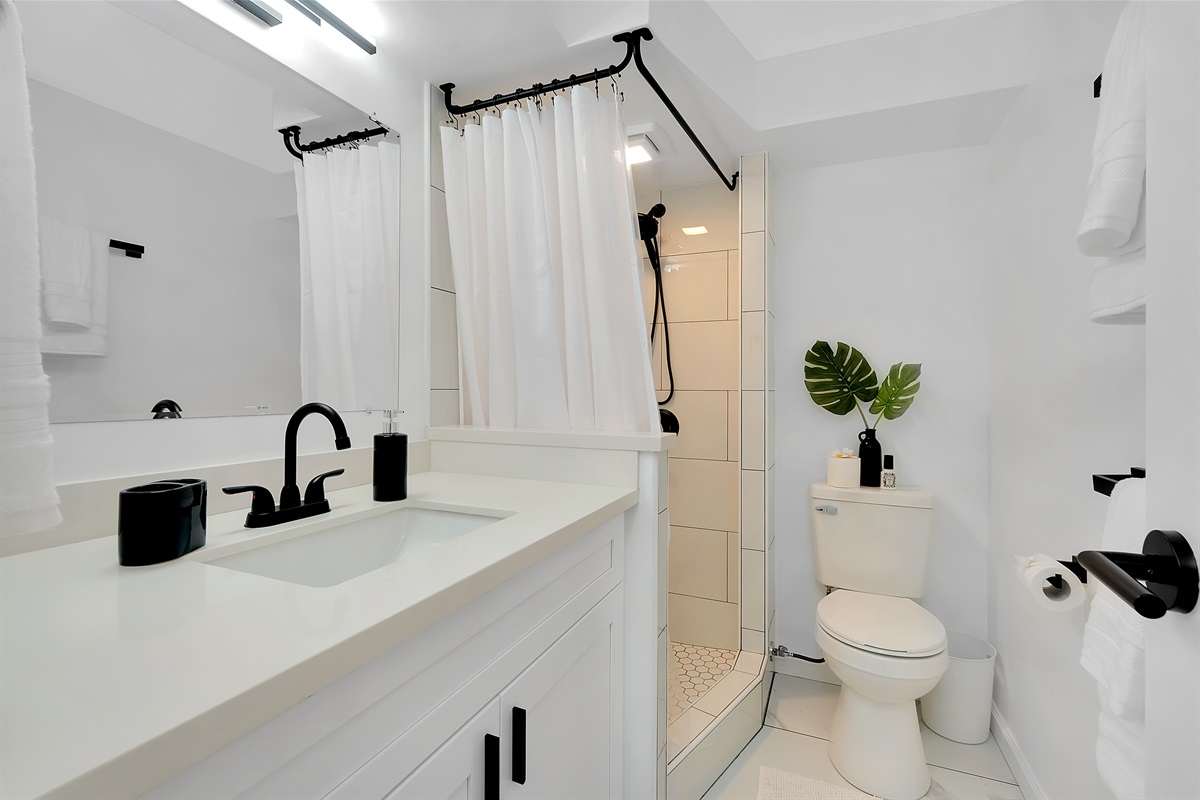Step into a spa-inspired retreat — this modern bathroom features a walk-in shower, sleek black fixtures, and soft tropical accents for a clean, calming island feel. Perfect for refreshing after a day exploring Waikīkī’s beaches and shops.