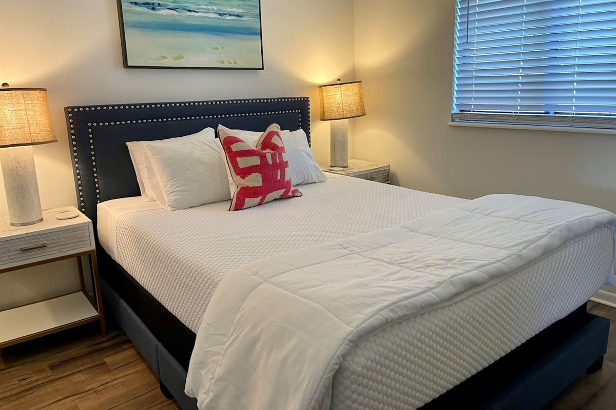 Serene and stylish bedroom with a plush king bed, crisp white linens, and calming coastal decor. Enjoy the glow of warm bedside lighting and blackout blinds for restful sleep—your perfect retreat after a day of adventure or work.