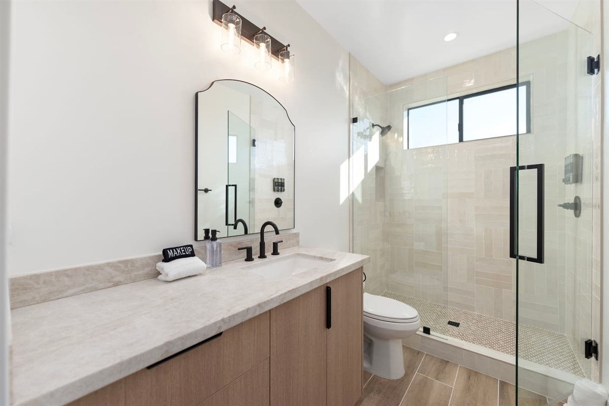 Bright and modern bathroom featuring a spacious glass-enclosed shower, sleek vanity with black fixtures, and plenty of counter space.