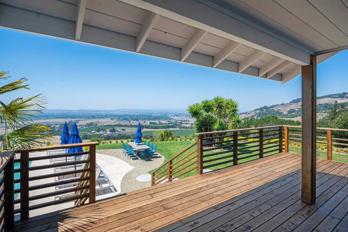 Large deck connects the kitchen and pool table room to the outdoor dining table, pool and spa, and lawn.