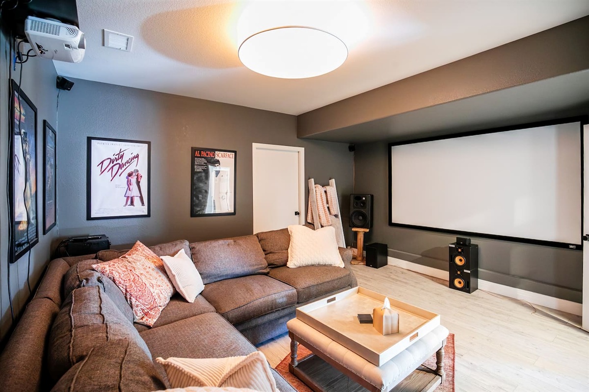 Family Movie Night!  This cozy movie theatre room features a large projection screen with surround sound speakers, creating the perfect movie-night setup. A plush sectional sofa offers comfortable seating to lounge after a long day!