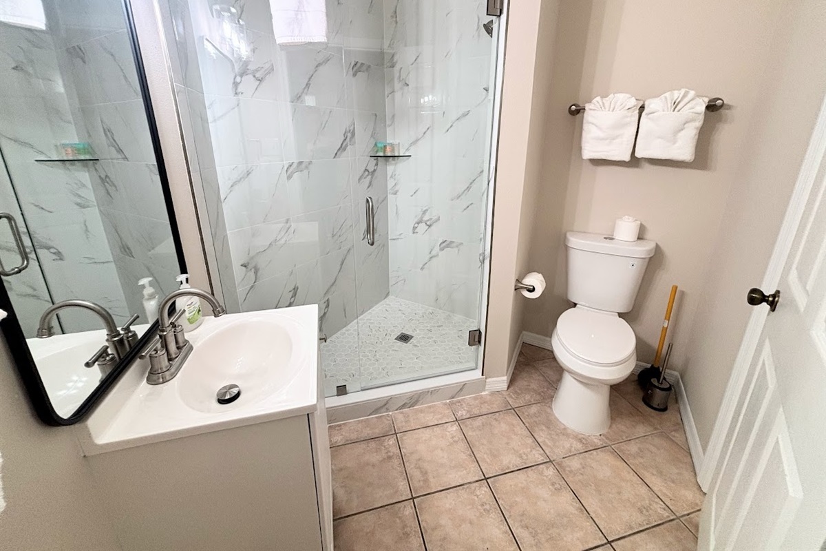 Updated bathroom featuring a glass-enclosed walk-in shower, vanity, toilet, and tile flooring.