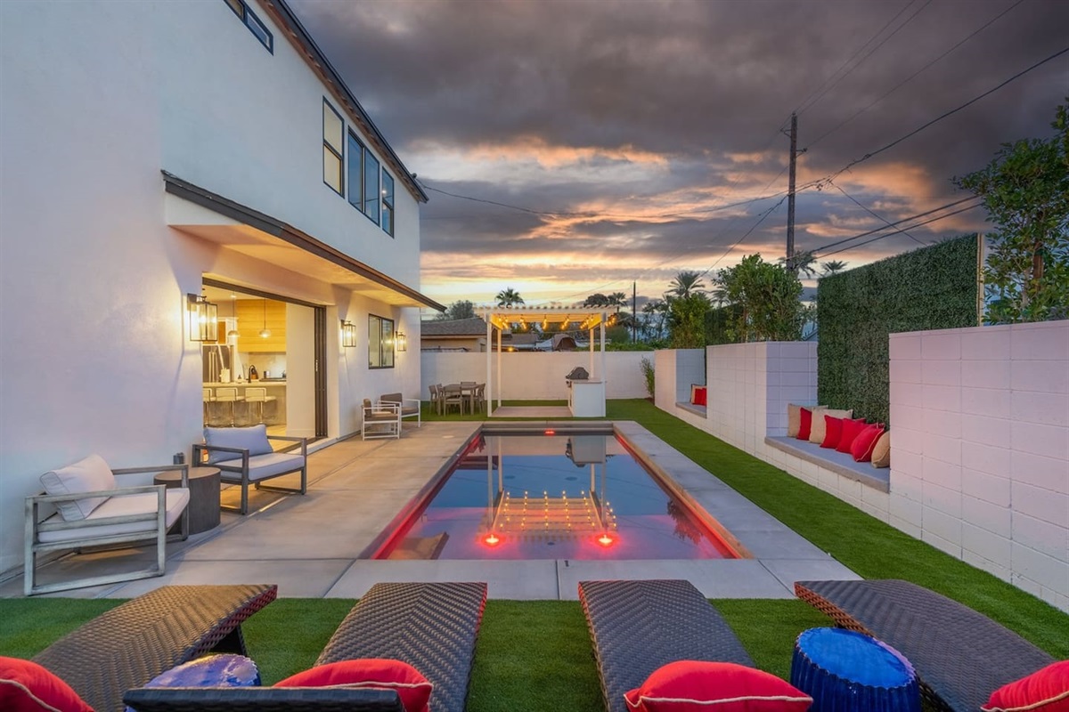 The enchanting pool area at night offers a relaxing ambiance with ample seating, a pergola with a grill, and dining tables, perfect for intimate gatherings or celebrations.
