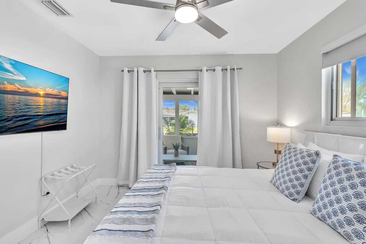 Bright and comfortable bedroom with a plush bed, Smart TV, ceiling fan, and plenty of natural light.