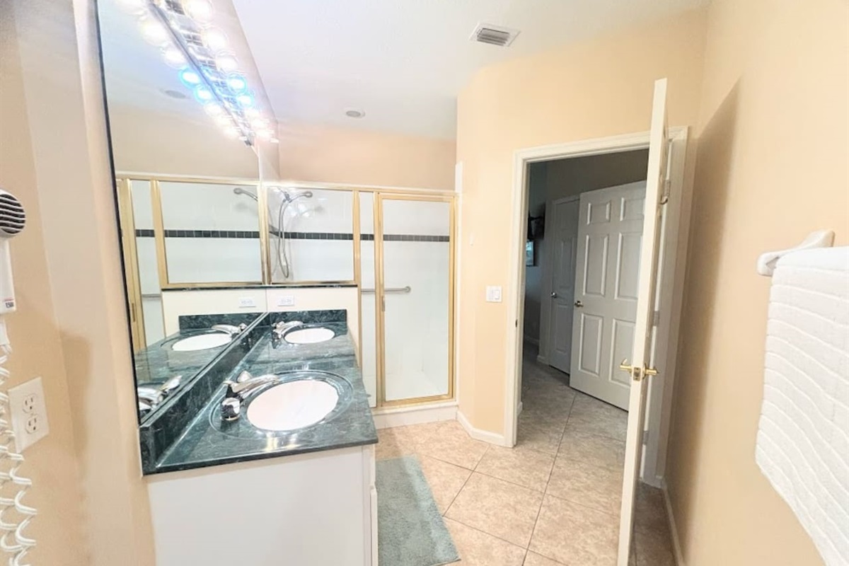 Bright bathroom with large vanity, full mirror, tile flooring, and a walk-in shower with glass doors.