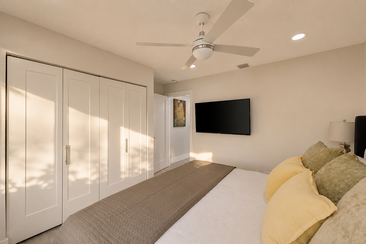 A clean king bedroom with a wall-mounted TV, ceiling fan, and closet space gives guests a simple, comfortable place to unwind.