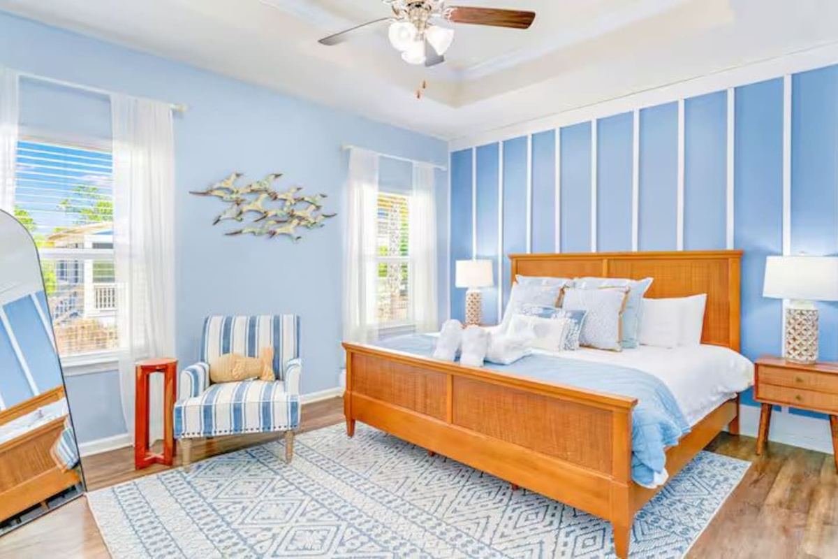 Unwind in this beautifully designed king bedroom featuring ceiling fan, bedside lamps, couch, and relaxing beach-inspired decor