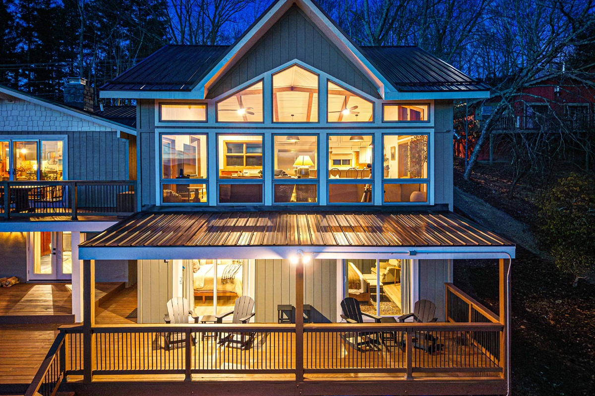 Evening exterior view of the home showcases the new side of the house glowing warmly against the mountain backdrop, with multiple deck levels designed for outdoor living.
